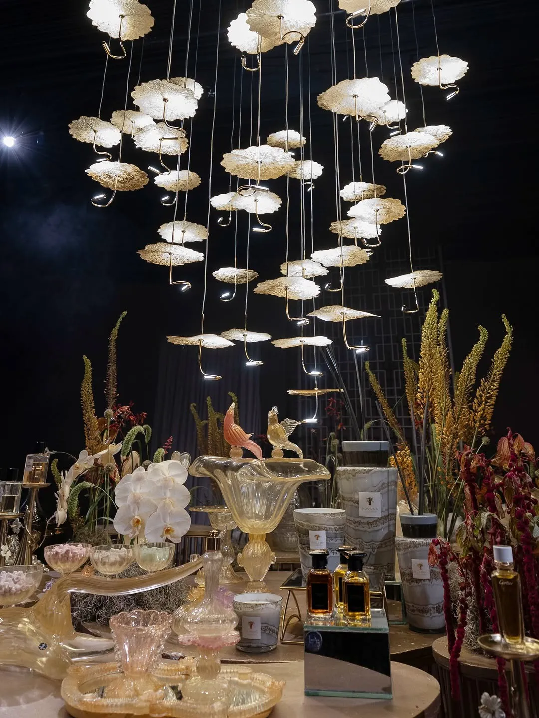 Hanging gold installation glowing above a hospitality table with fragrance and sweets