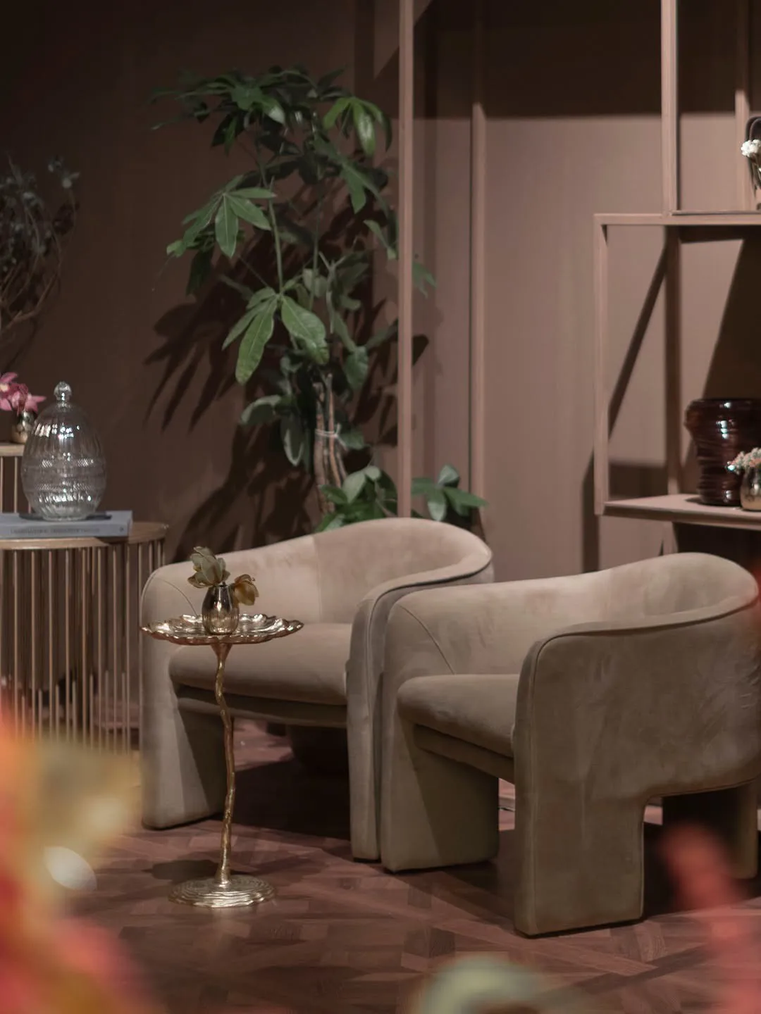 Velvet armchairs beside a gold side table and greenery