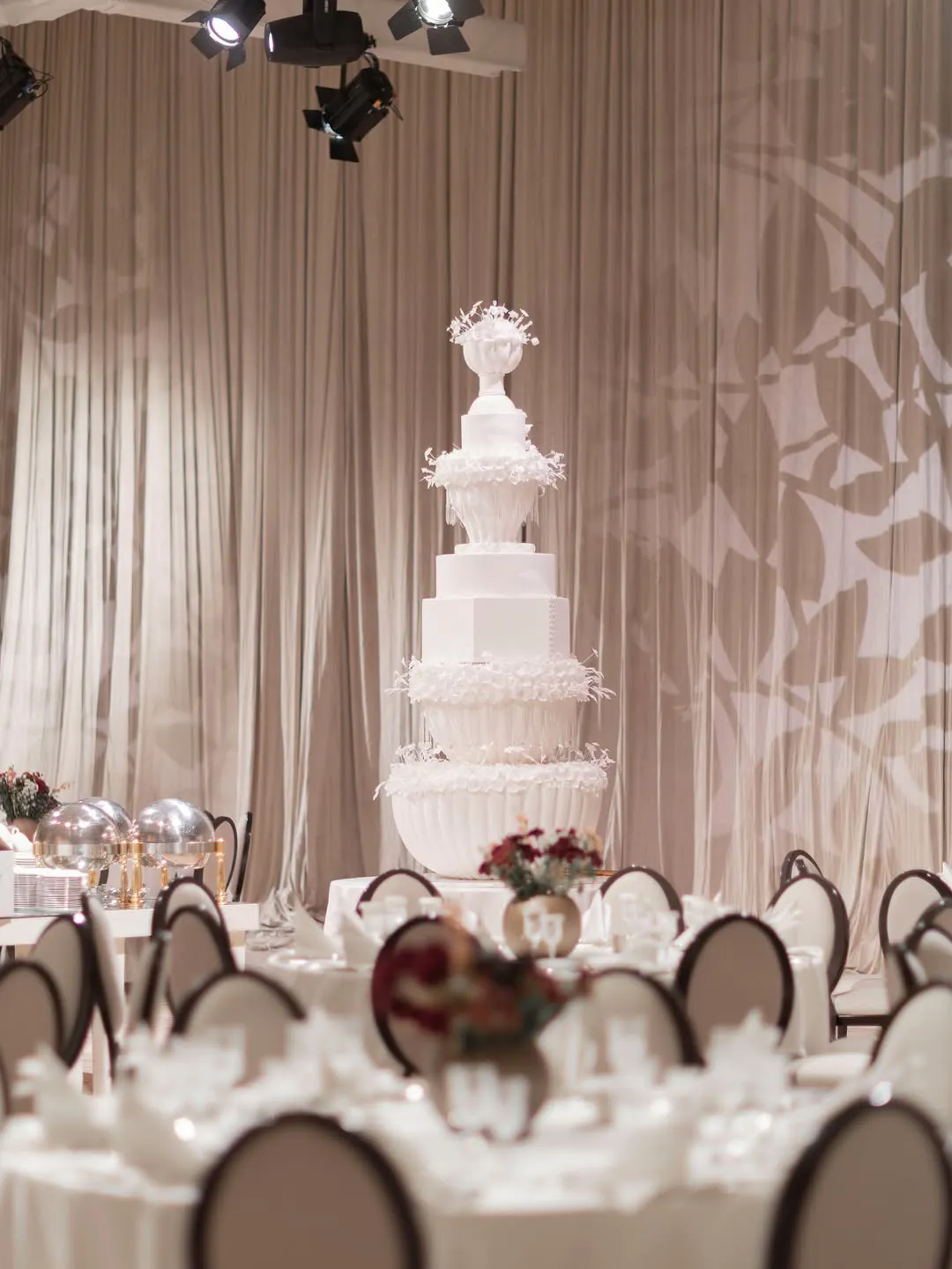 Tiered wedding cake on stage beside round tables dressed in white