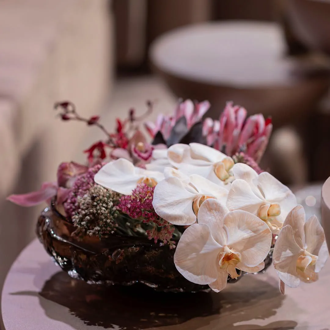 White orchids and pink protea arranged in an amber glass bowl