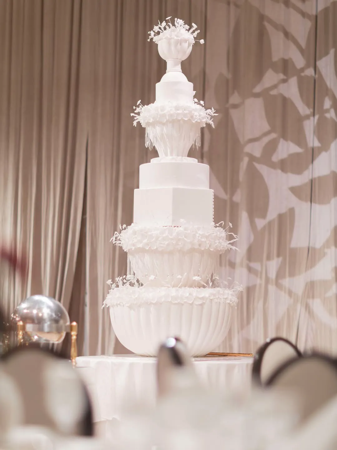 Tall tiered white wedding cake set against draped fabric