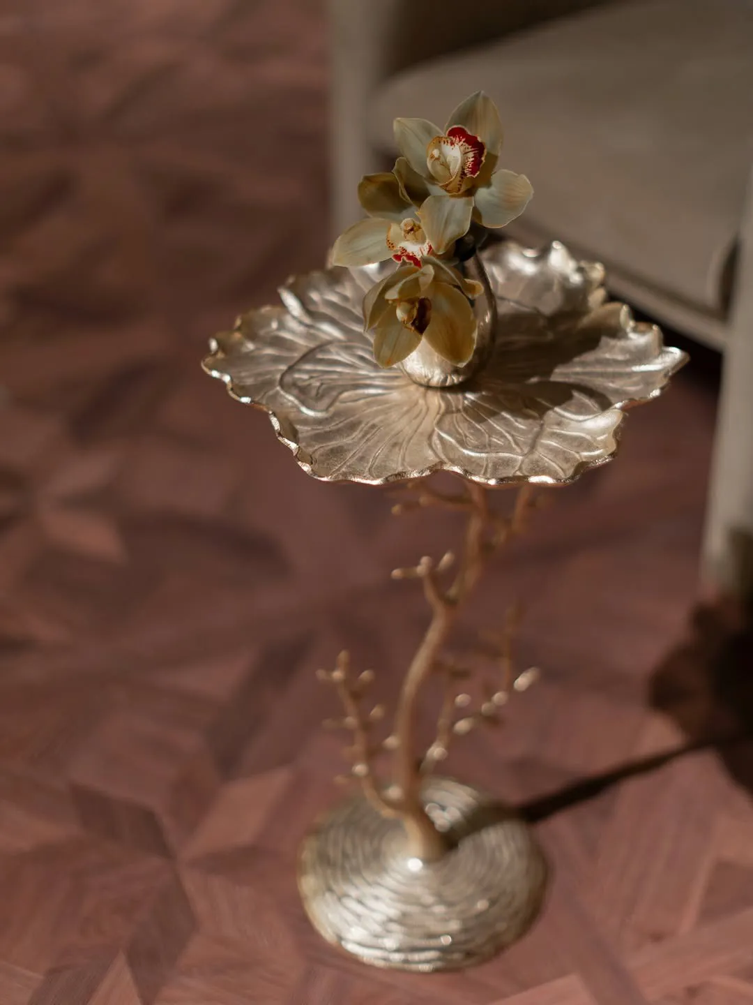 Gold leaf-shaped stand holding an orchid, on a parquet floor